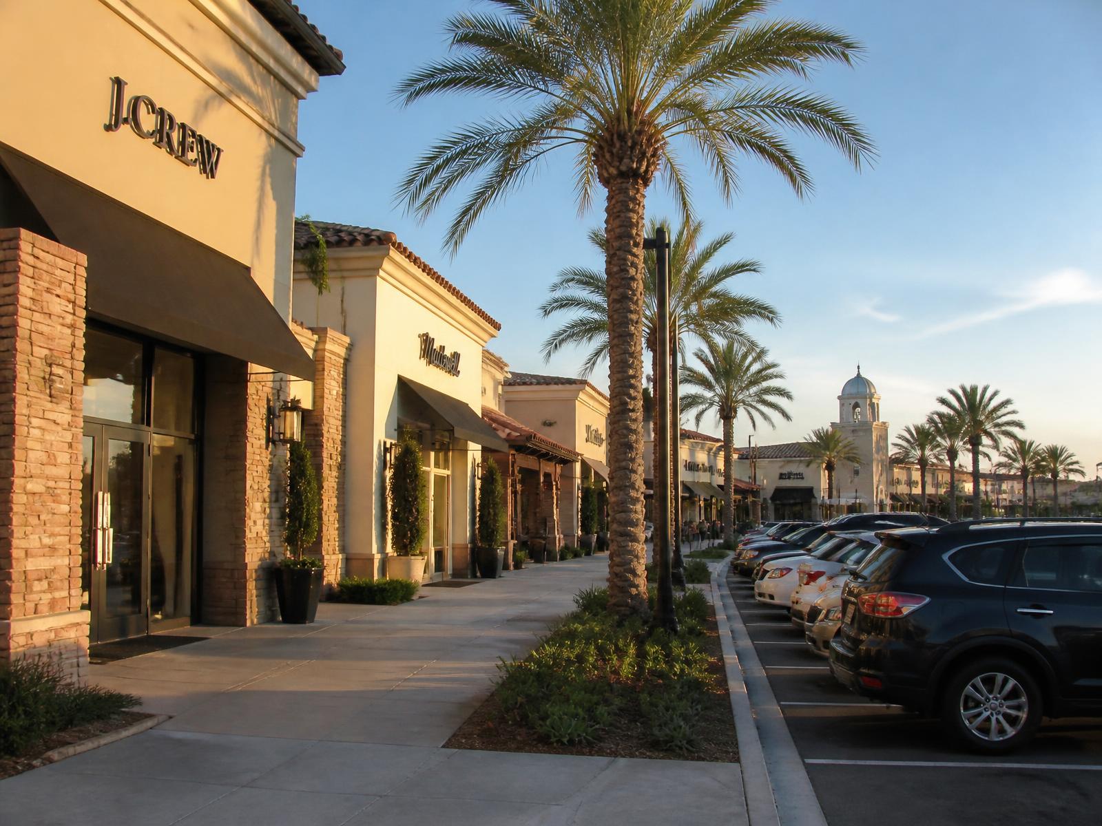 Southern California open-air strip mall retail center with stucco storefronts, awnings and palm-lined walkway